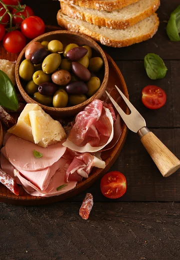 photo d'aliments disposés sur une table, olives, fromage, tomates et jambon sec