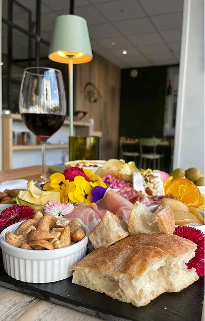 Photo d'une table sur laquelle se trouve un verre de vin rouge ainsi qu'un plateau de nourriture à partager