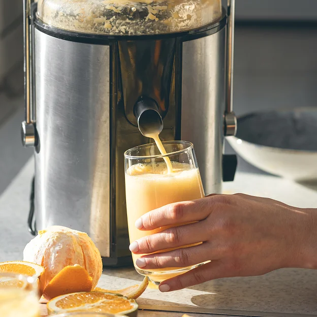 photo d'une personne en train de tenir un verre et en train de se servir du jus à la centrifugeuse